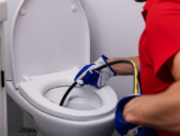 A plumber inserts a hydro jetting nozzle into a toilet to clear a drain blockage.