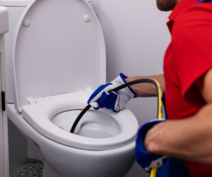 A plumber inserts a hydro jetting nozzle into a toilet to clear a drain blockage.