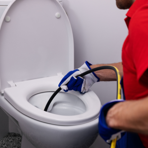 A plumber inserts a hydro jetting nozzle into a toilet to clear a drain blockage.