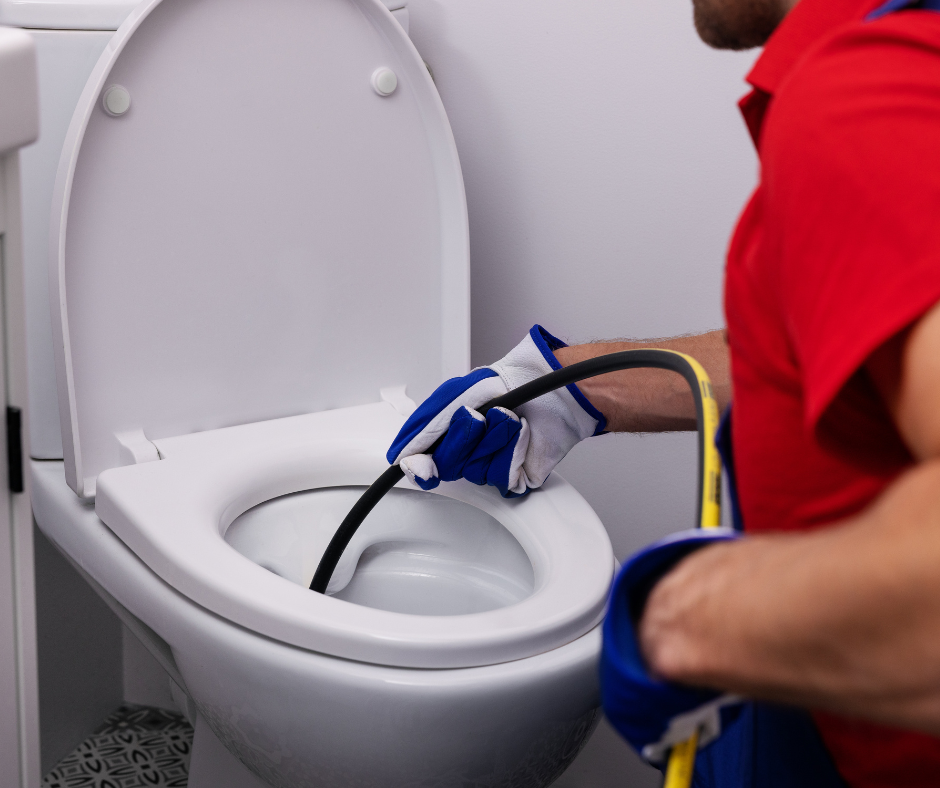 A plumber inserts a hydro jetting nozzle into a toilet to clear a drain blockage.