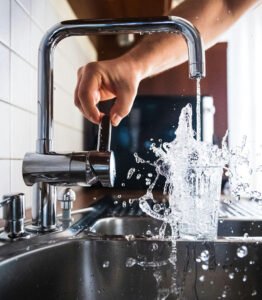 Person turning on a functioning kitchen faucet with smooth running water.